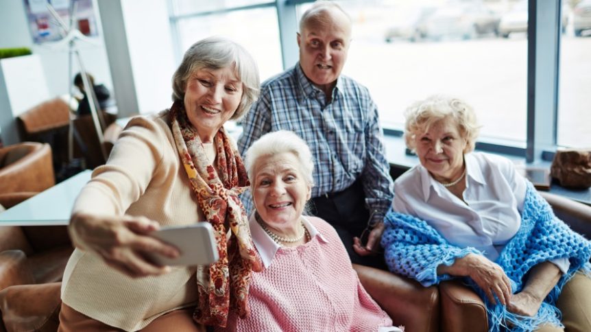 Group of carefree seniors with smartphone making selfie in cafe assisted living